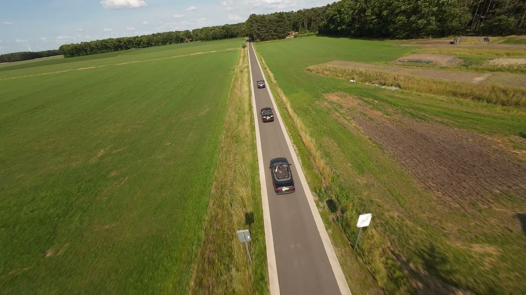 Drie Saab-cabrio's achter elkaar op een smalle weg tussen de velden