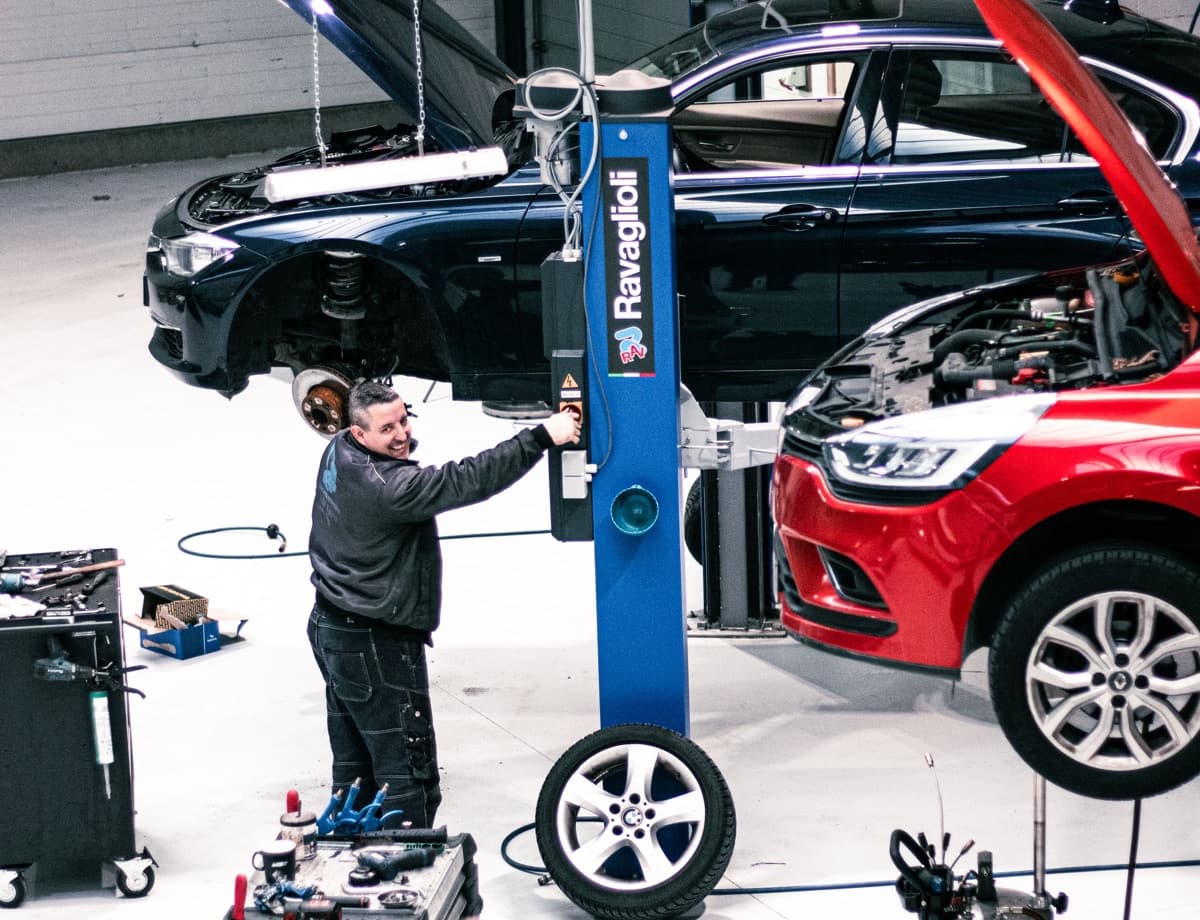 Technieker bedient de hefbrug onder een BMW 3-serie met het voorwiel eraf
